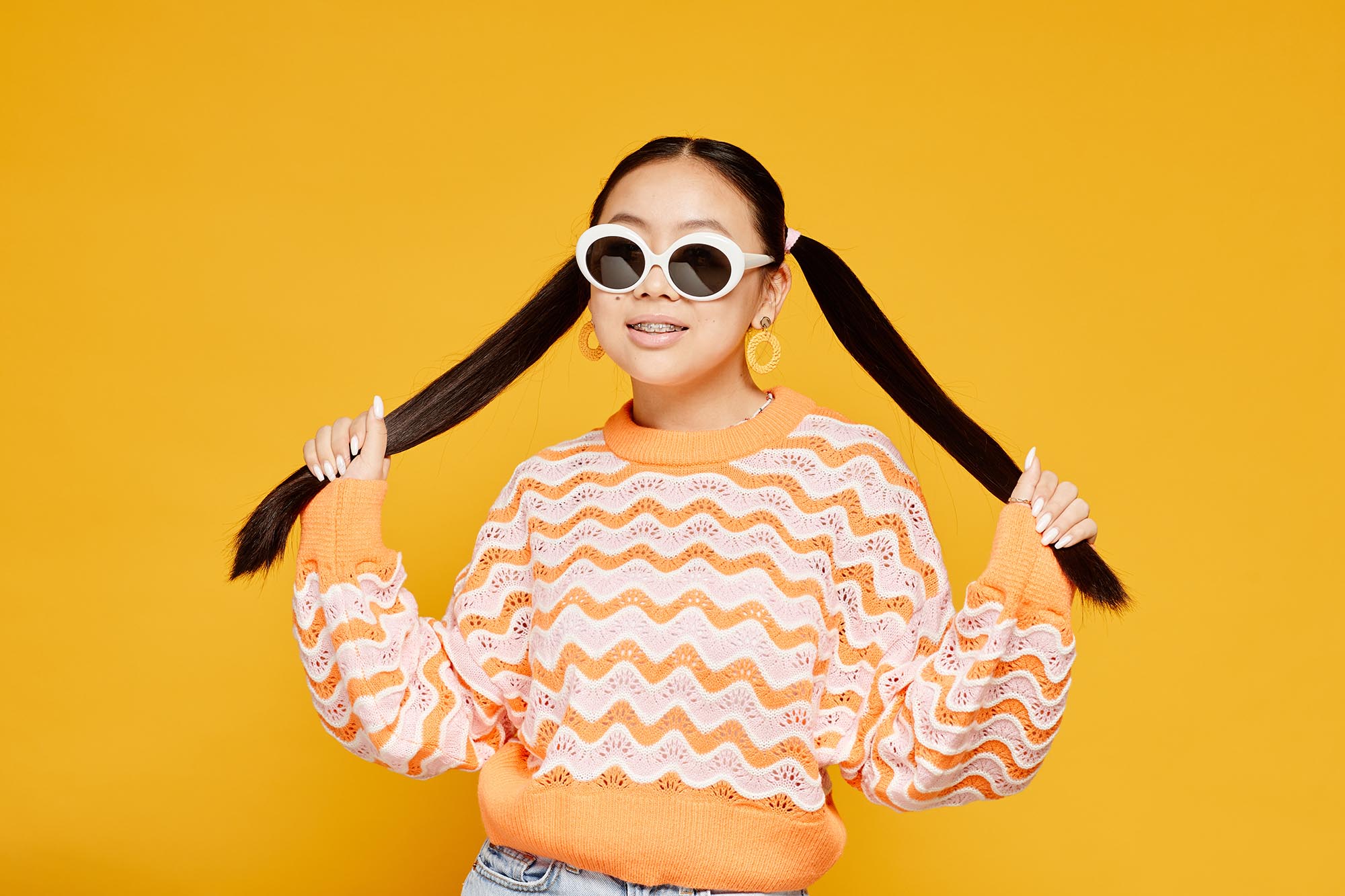 Waist up portrait of funky teenage girl with pigtails over colored yellow background