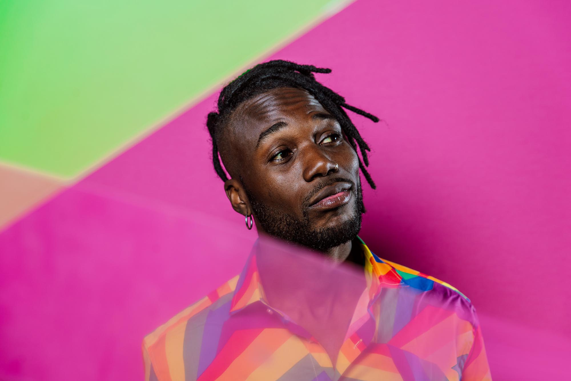artistic portrait of an African American man wearing colorful shirt posing on pink and green backgrounds