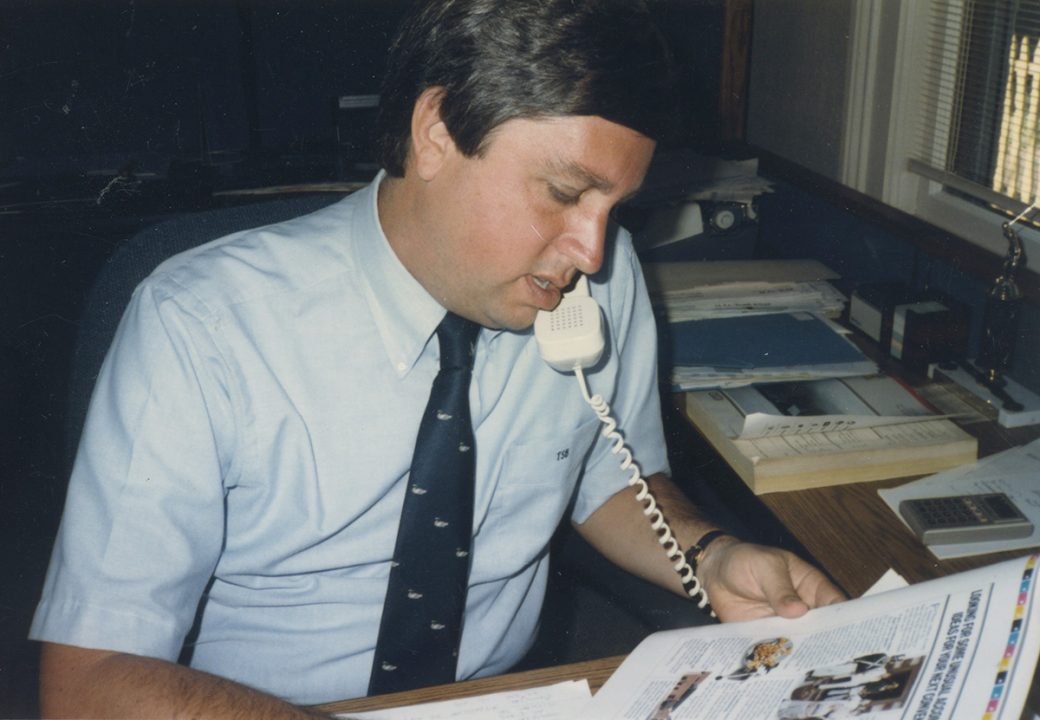 Tim Borne, Asher Agency founder, reviewing printer proofs while talking on a telephone.