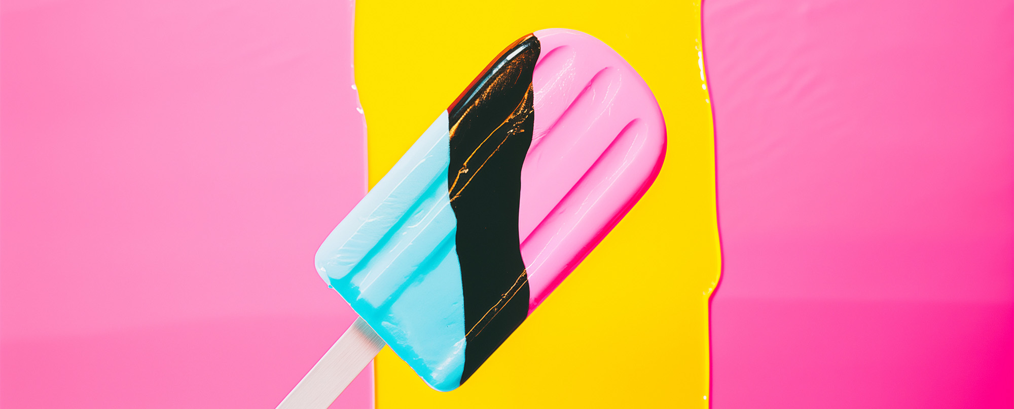 A blue, black and pink popsicle on a white stick against yellow and pink background. Minimalist and abstract feel.