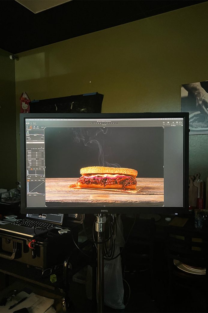 A bbq brisket sandwich is shown on a digital monitor on set at a photoshoot. There is steam rising from the sandwich on screen.