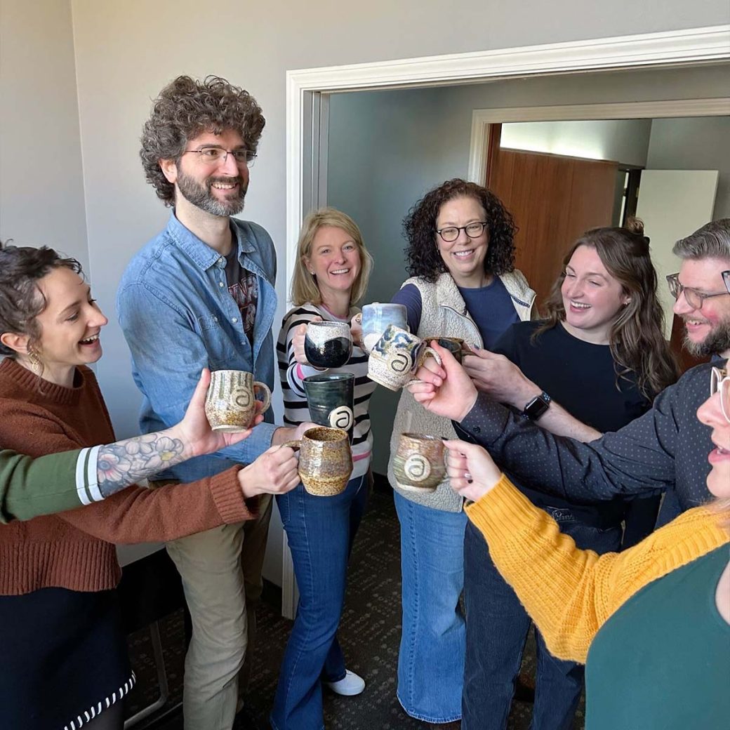 Asher team members cheers custom-made ceramic mugs with the letter "a" on them.
