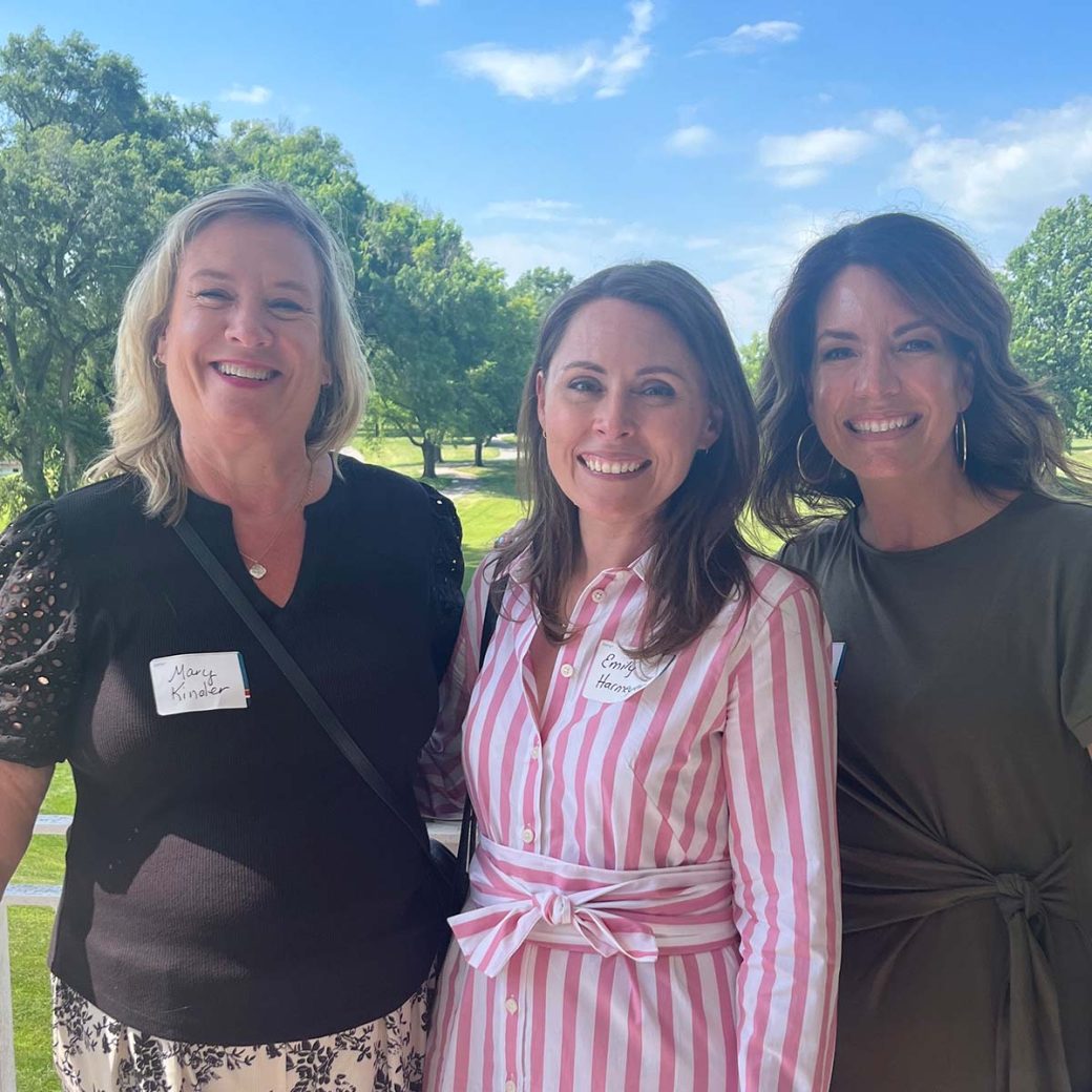 Mary Kinder, Emily Harmeyer and Jennifer Roberts pose for a picture in front of trees and blue, cloudy skies